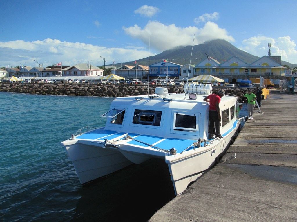 A white ferry tied up at the Charlestown pier, with Nevis Peak in cloud behind the town
