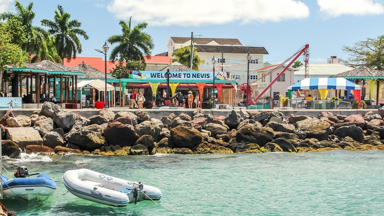 The Charlestown ferry pier on Nevis, with a "Welcome to Nevis" sign over the waterfront and small boats in the clear water