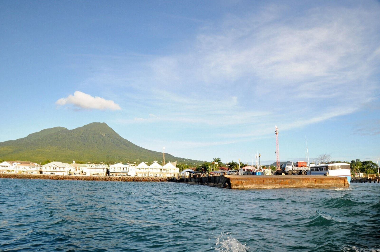 Charlestown's waterfront seen from the sea, with Nevis Peak rising green behind the town
