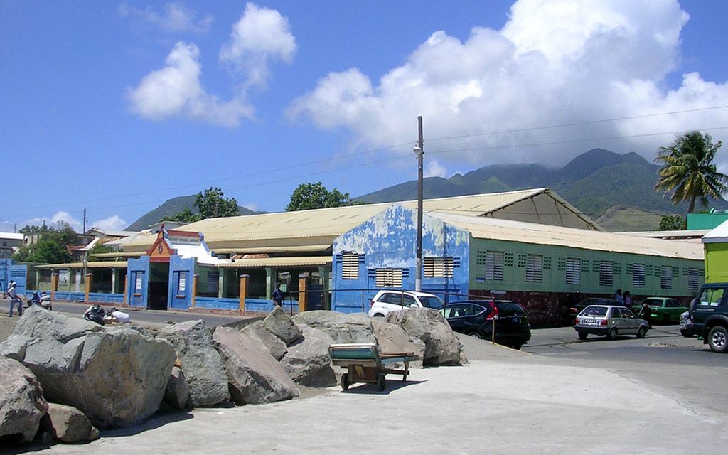 The public market building on the Basseterre waterfront, painted blue and green, with green mountains behind it