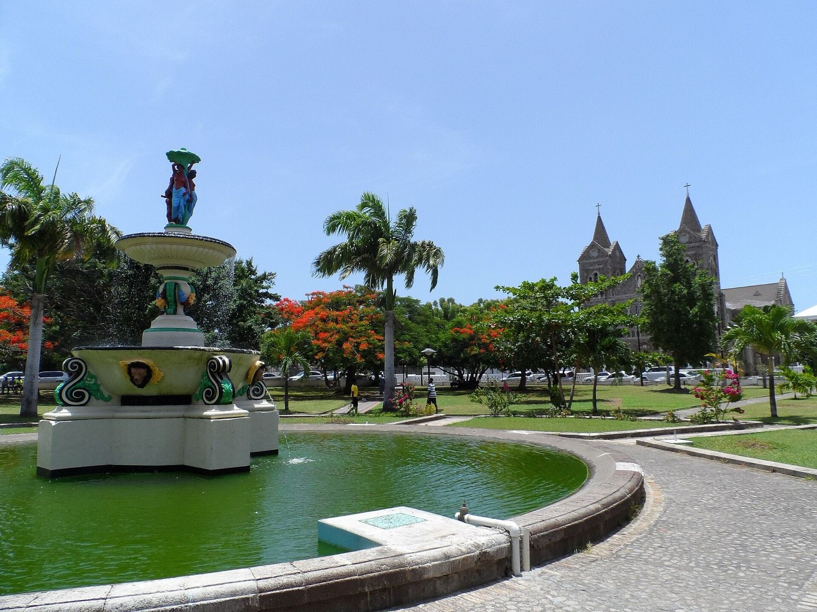 The fountain in Independence Square, Basseterre, with flame trees in bloom and the stone towers of the Co-Cathedral behind