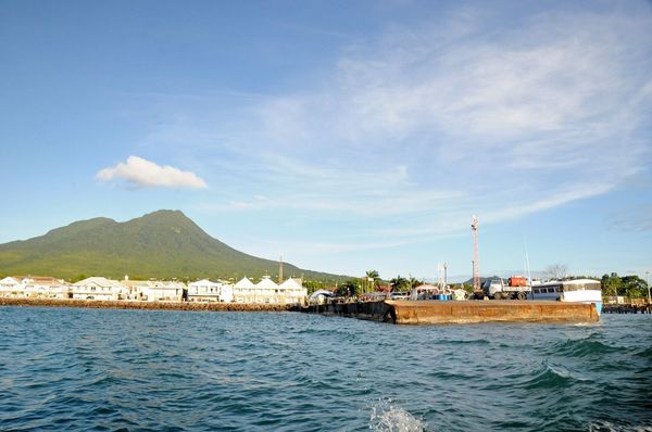 Charlestown's waterfront seen from the sea, with Nevis Peak rising green behind the town