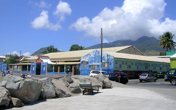 The public market building on the Basseterre waterfront, painted blue and green, with green mountains behind it