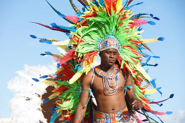 A masquerader in a towering headdress of green, orange and blue feathers at Sugar Mas in St. Kitts